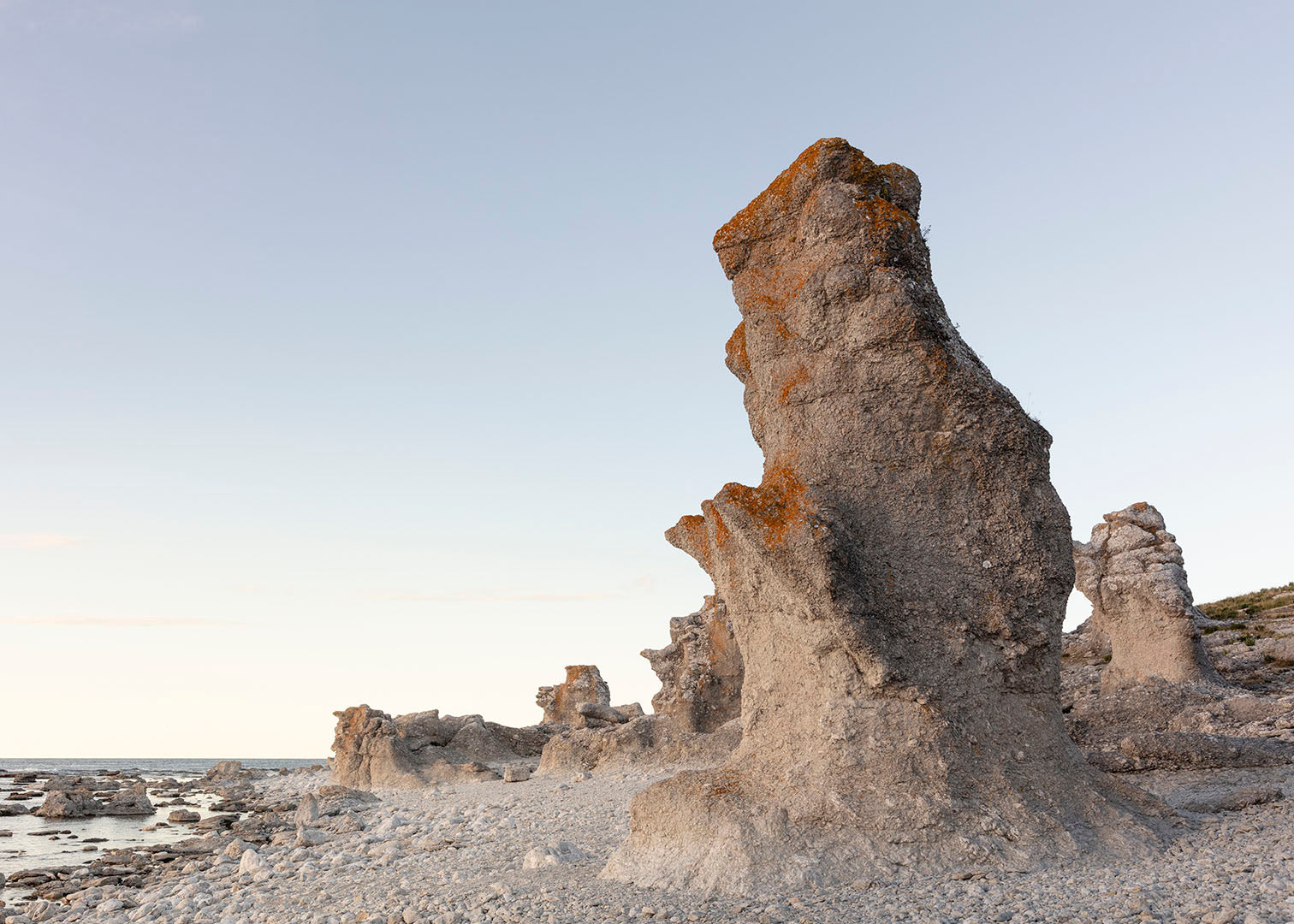 Kunst fotografi af Langhammarsgubben rauk på Fårö, Gotland i blødt aftenlys med kystlinje i baggrunden.